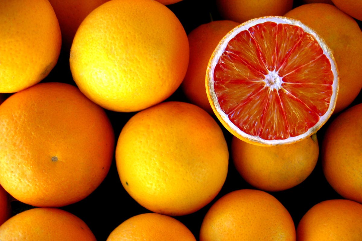 A sliced orange lies face-up on a pile of uncut fruit.