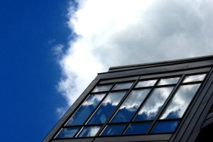 A cloud in a blue sky is reflected in the windows of a modern building.