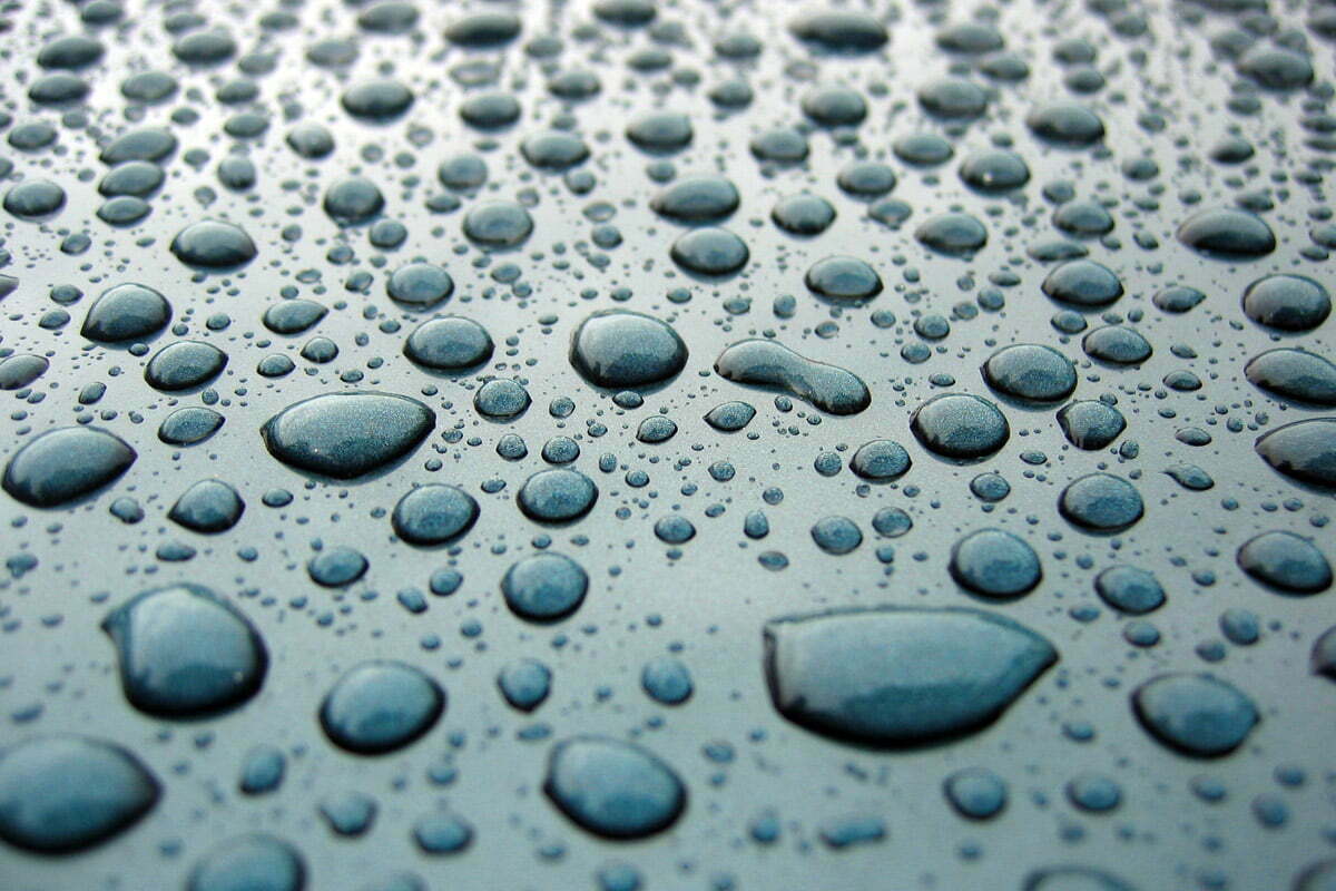 Hundreds of raindrops close-up isolated on the hood of a car.