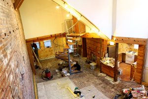The panoramic view of the basement apartment under renovation with tool and equipment strewn across the floor. As seen from loft bedroom.