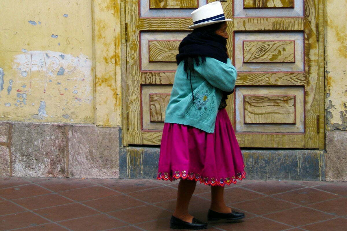 An Ecuadorian woman in traditional colorful dress walks down the street. 