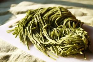 Green pasta lies in a pile on a cutting board.