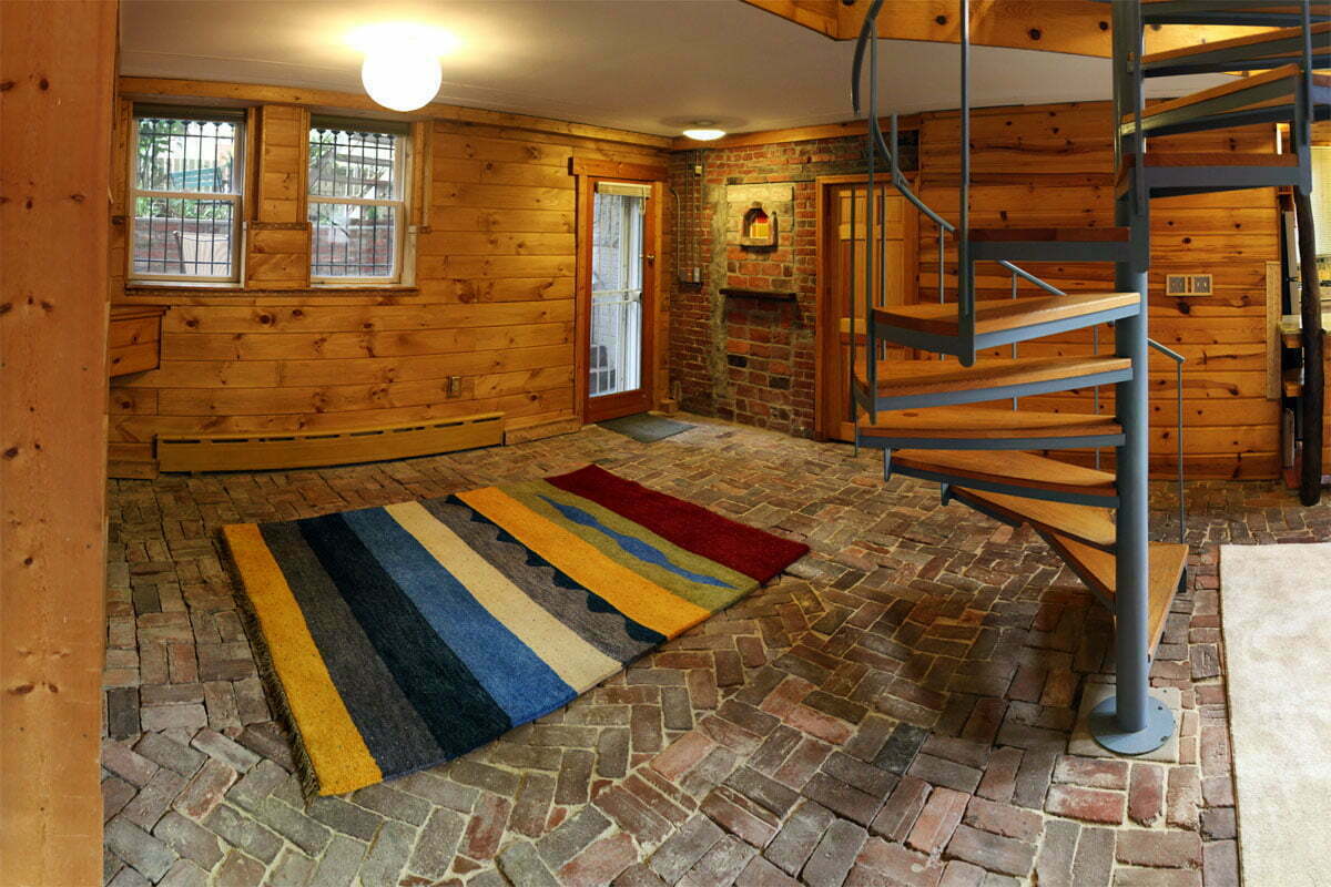 A panoramic photo of the front area of a basement apartment with a large rug and spiral staircase.