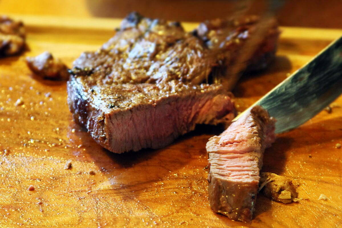 A grilled medium rare steak being sliced open on a wooden cutting board.