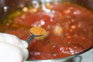 A teaspoon of cayenne pepper dangling over a pot of tomato sauce.