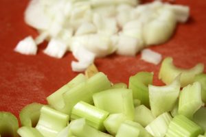 Two distinct piles of chopped celery and onions lie on a red cutting board.