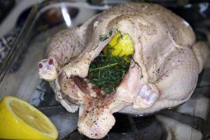 A chicken in a pan before going into the oven, covered in spices and stuffed with vegetables.