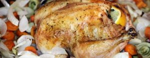 A chicken roast freshly taken out of the oven with spices and veggies surrounding it.
