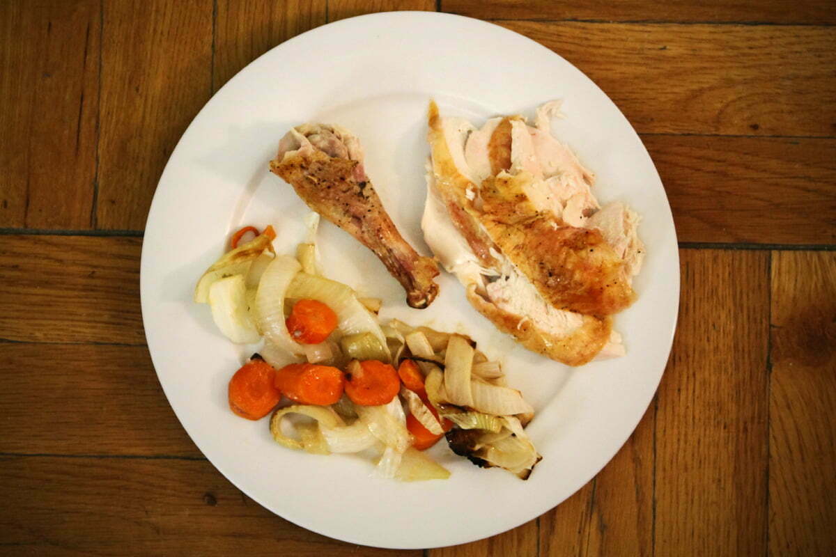 A white plate full of roast chicken with a drumstick and assorted veggies.