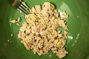 A pile of tuna lies in a green bowl with a fork coming in from the side.