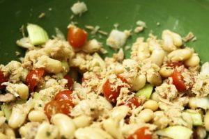 A close-up photo of a tuna salad in a green bowl with tomatos, onions, celery and fresh rosemary.