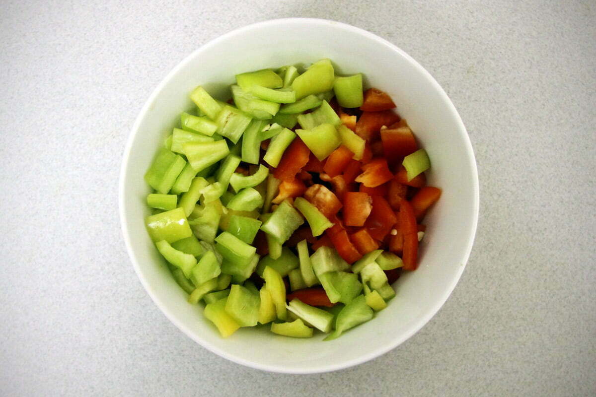 Sliced green peppers and cut red peppers sit in a white bowl.
