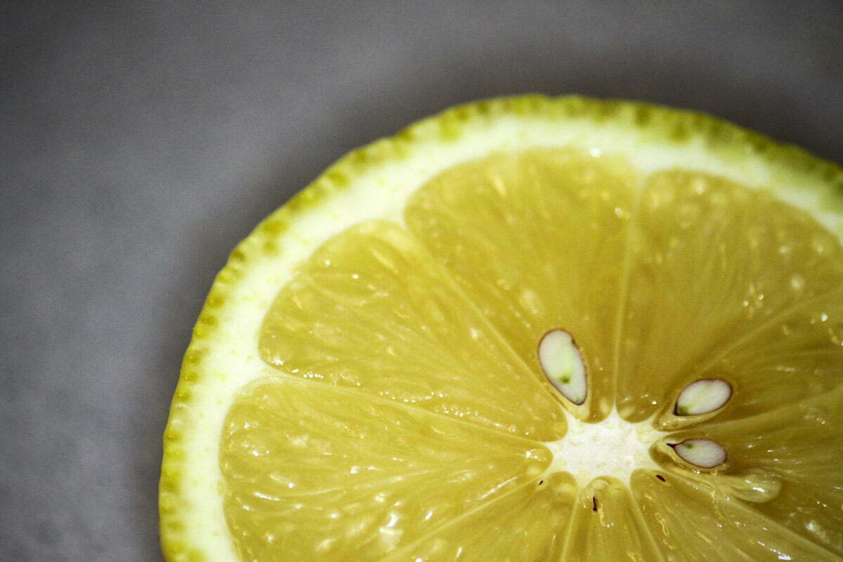 A closeup photo of a bright yellow lemon slice with seeds and detailed skin.