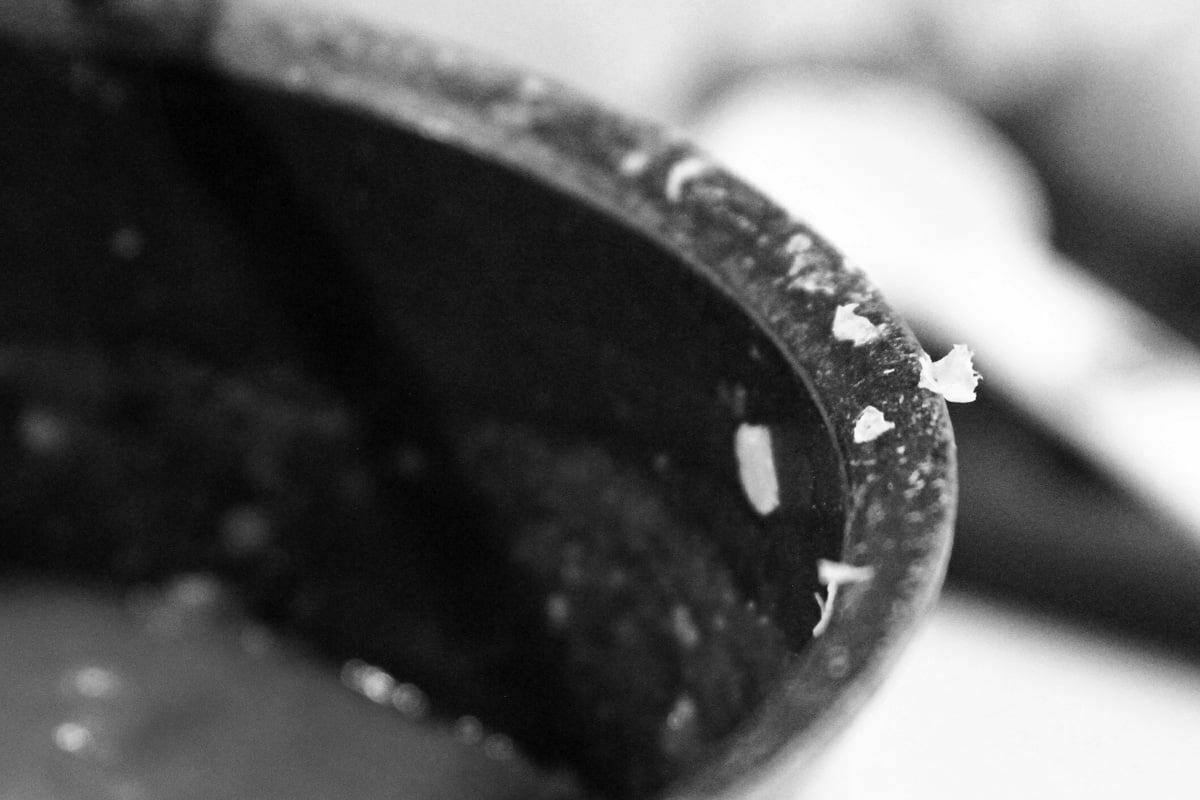 A focused black and white image of some slices of onion on the rim of a cooking pot.