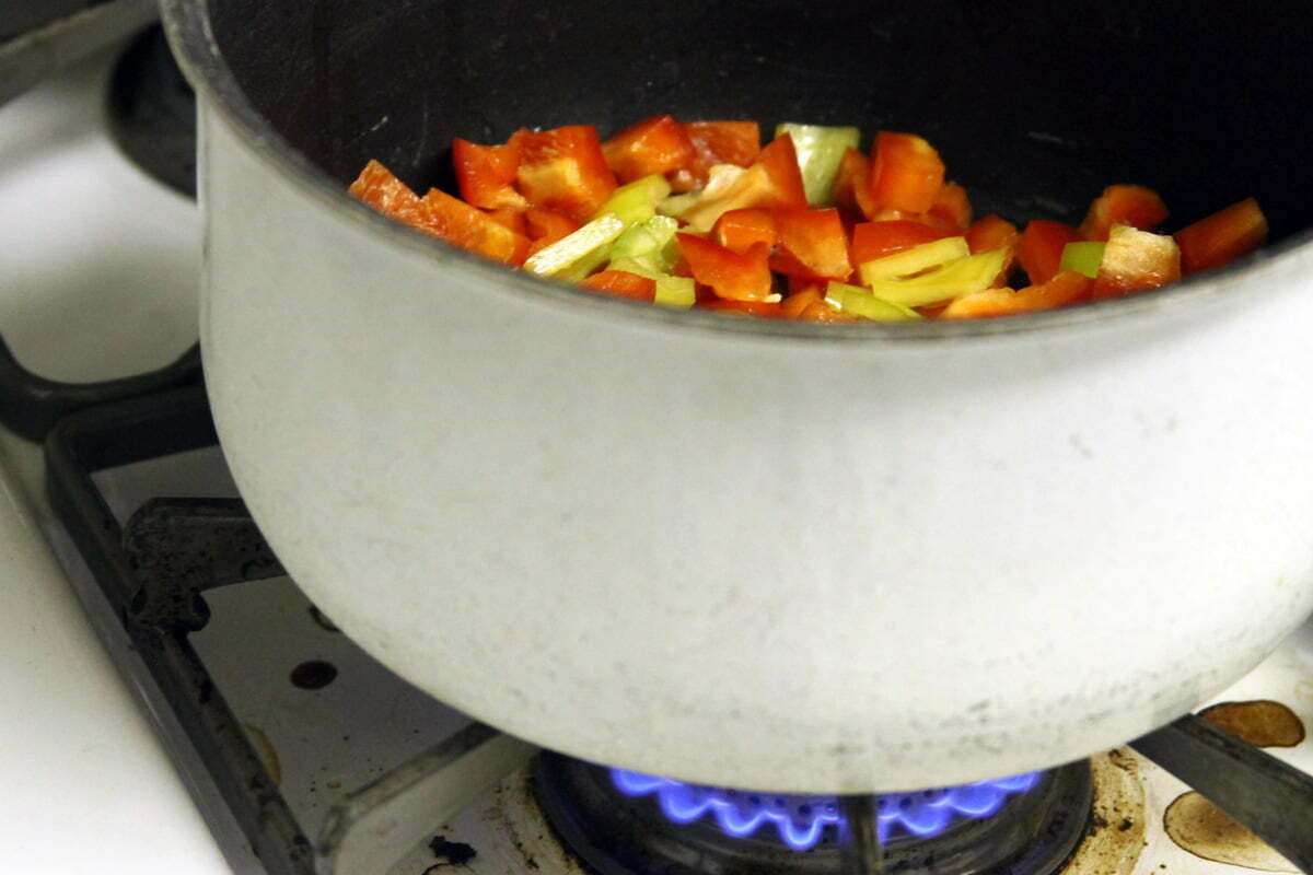 A white pot of colorful chopped veggies sits on the lit burner.
