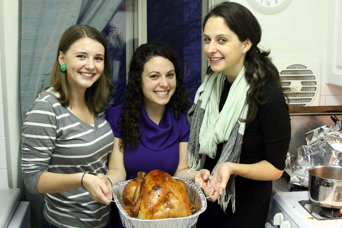 Three friends collectively hold up a thanksgiving turkey for the fakesgiving tradition.
