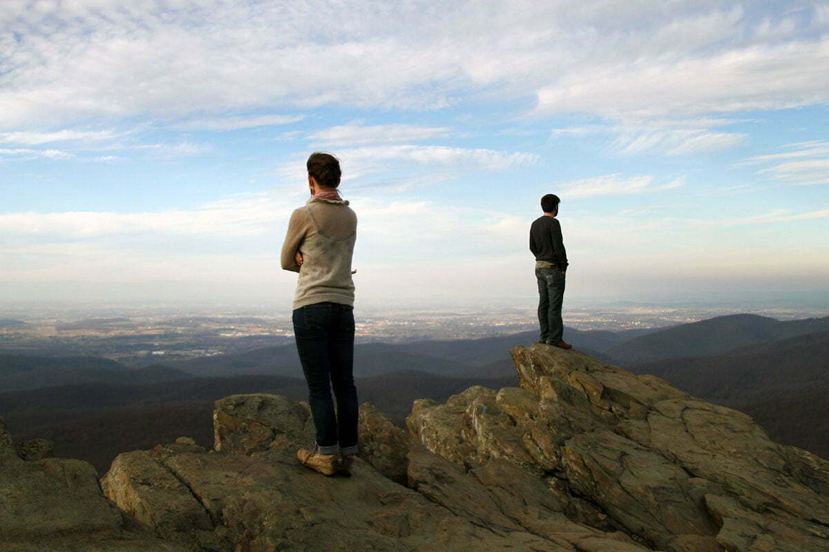 A man and woman face different directions looking out over a panoramic view.