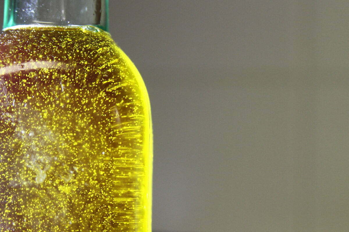 A close-up photograph of a bottle of olive oil with little air bubbles showing in the light.