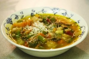 A bowl of momma's veggie soup with some parmesan cheese on top.
