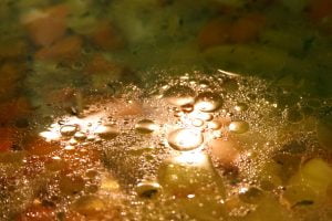 Light is reflected off of the oily surface of a vegetable soup being prepared in a large pot.