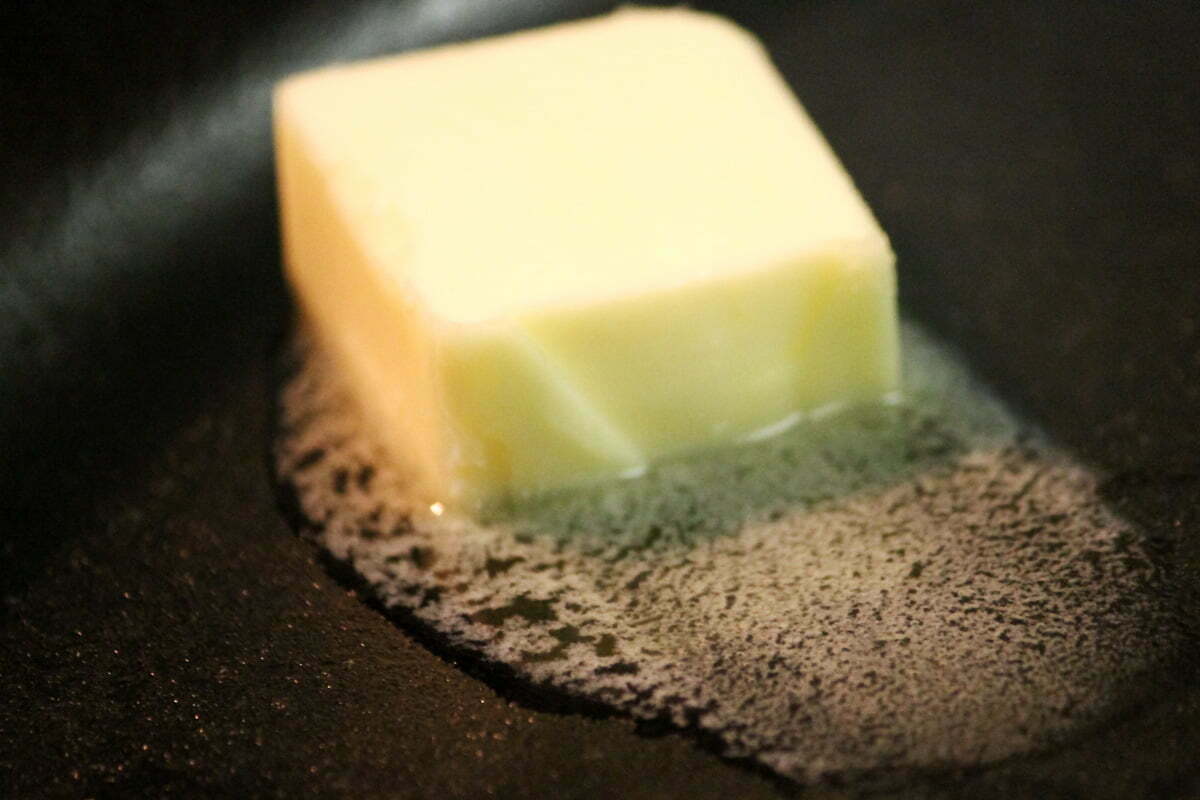 A big piece of butter starts to melt in a hot cast iron skillet.