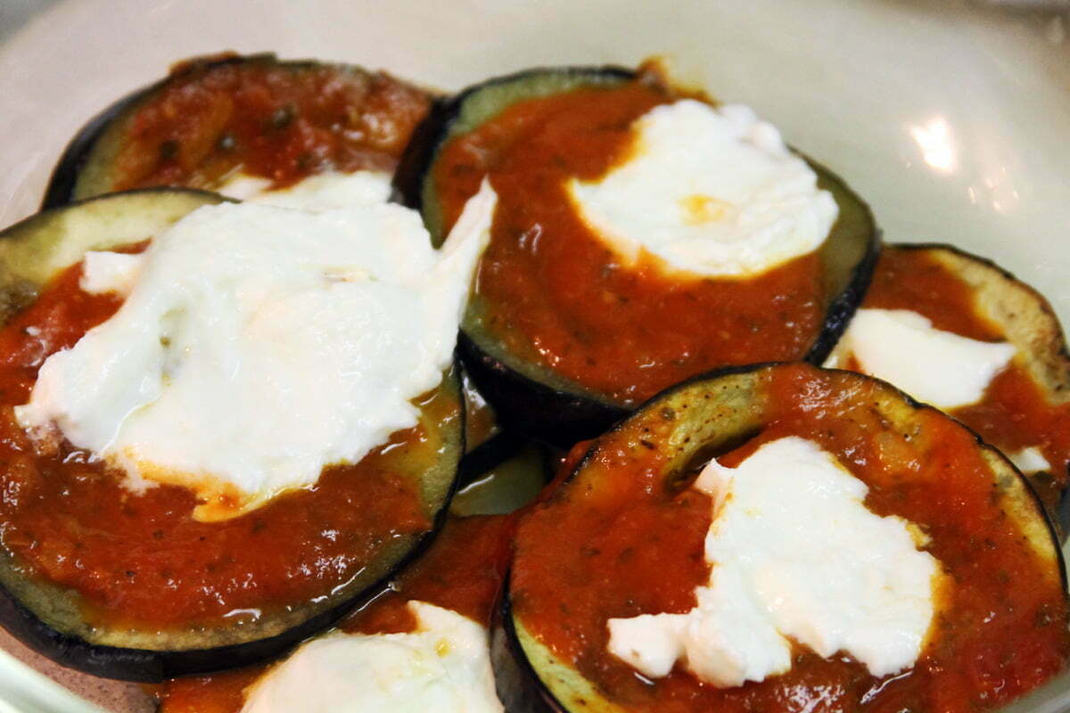 Mozzarella cheese is added to the eggplant slices with tomato sauce.