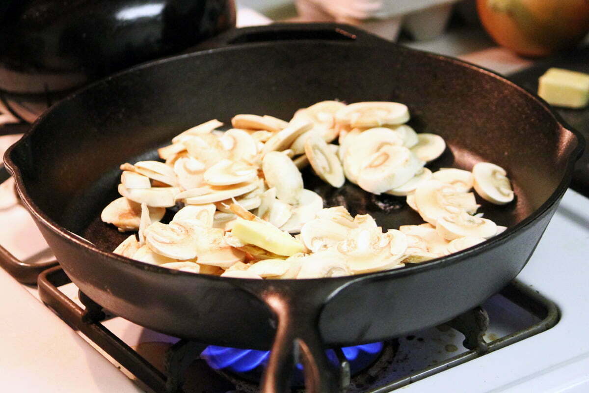 A pile of mushrooms cook in butter on a hot cast iron skillet.