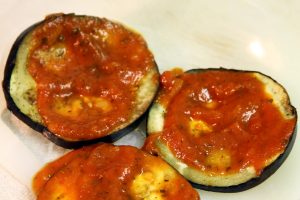 Dollops of red tomato sauce are put on the pieces of eggplant.