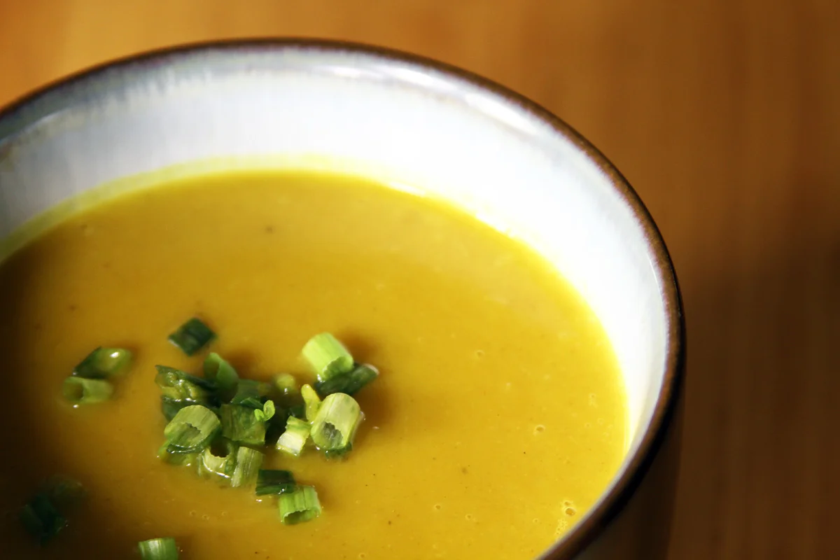 A close-up photograph of a large cup of butternut squash soup.