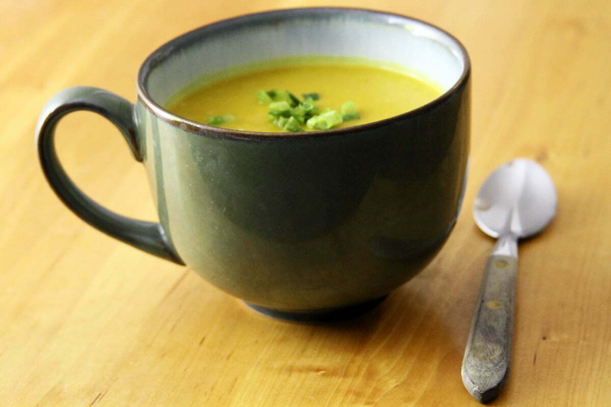 A side angle of a bowl filled with butternut squash soup and a spoon on a wooden table.