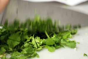 A blurred kitchen knife cuts into a pile of bright green cilantro herbs.