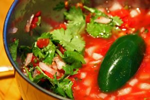 Homemade salsa made with a large green jalapeño pepper sits in a bowl with onions, tomatos and cilantro.