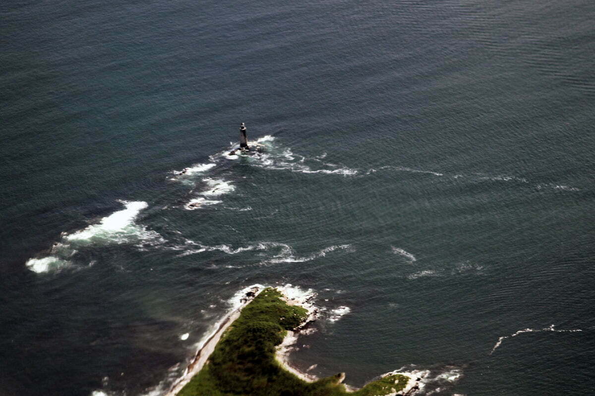 A lighthouse in Maine near the coast with waves surrounding it seen from an airplane.