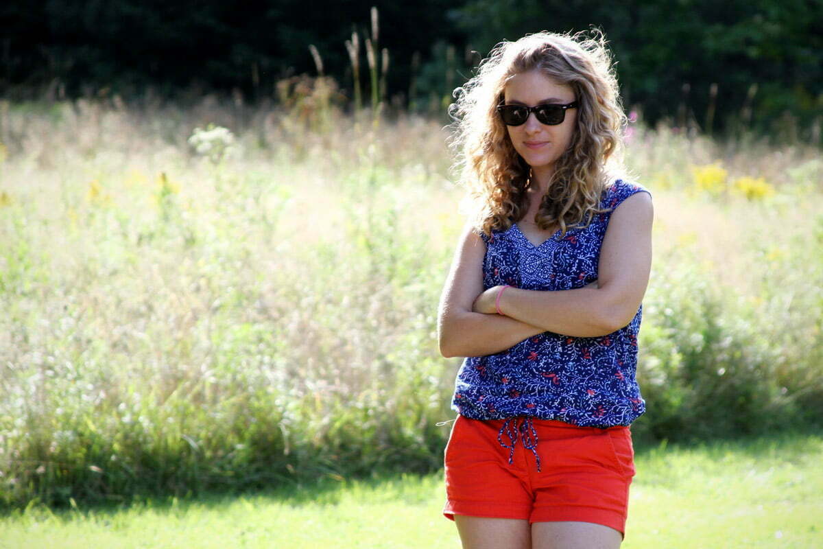 A girl in sunglasses stands wearing colorful clothes with her arms crossed in a field of wild flowers in Maine.