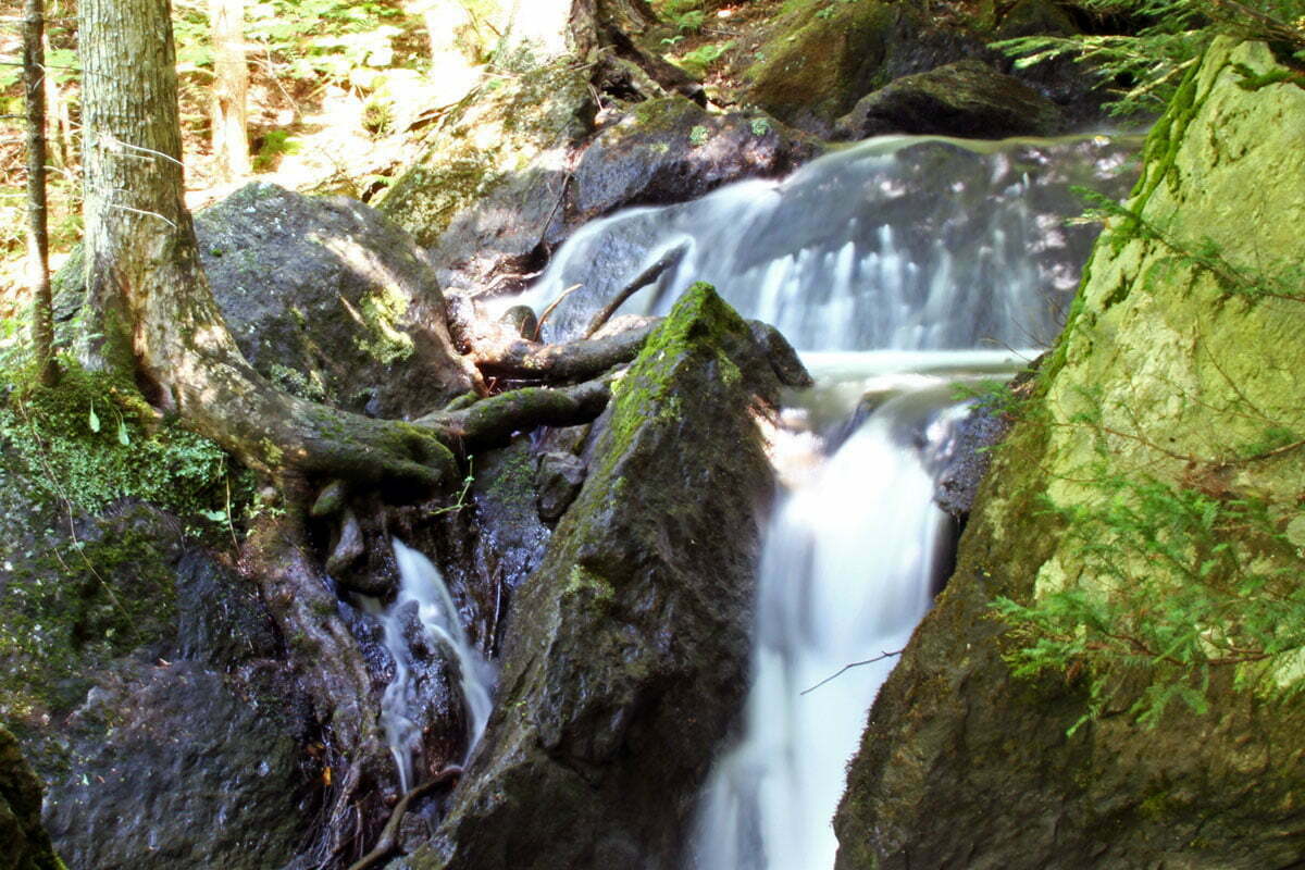 A long time-lapse photo of a water fall in the woods of Vermont.