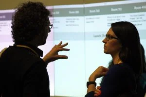 A photograph of two people in conversation in front of a projector screen at the Sunlight Foundation's TransparencyCamp.