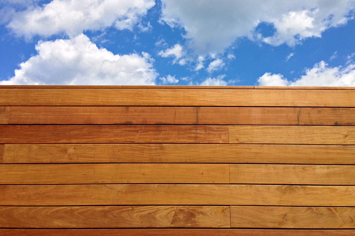 Photograph of a blond wooden wall with a cloud filled blue sky in the background.