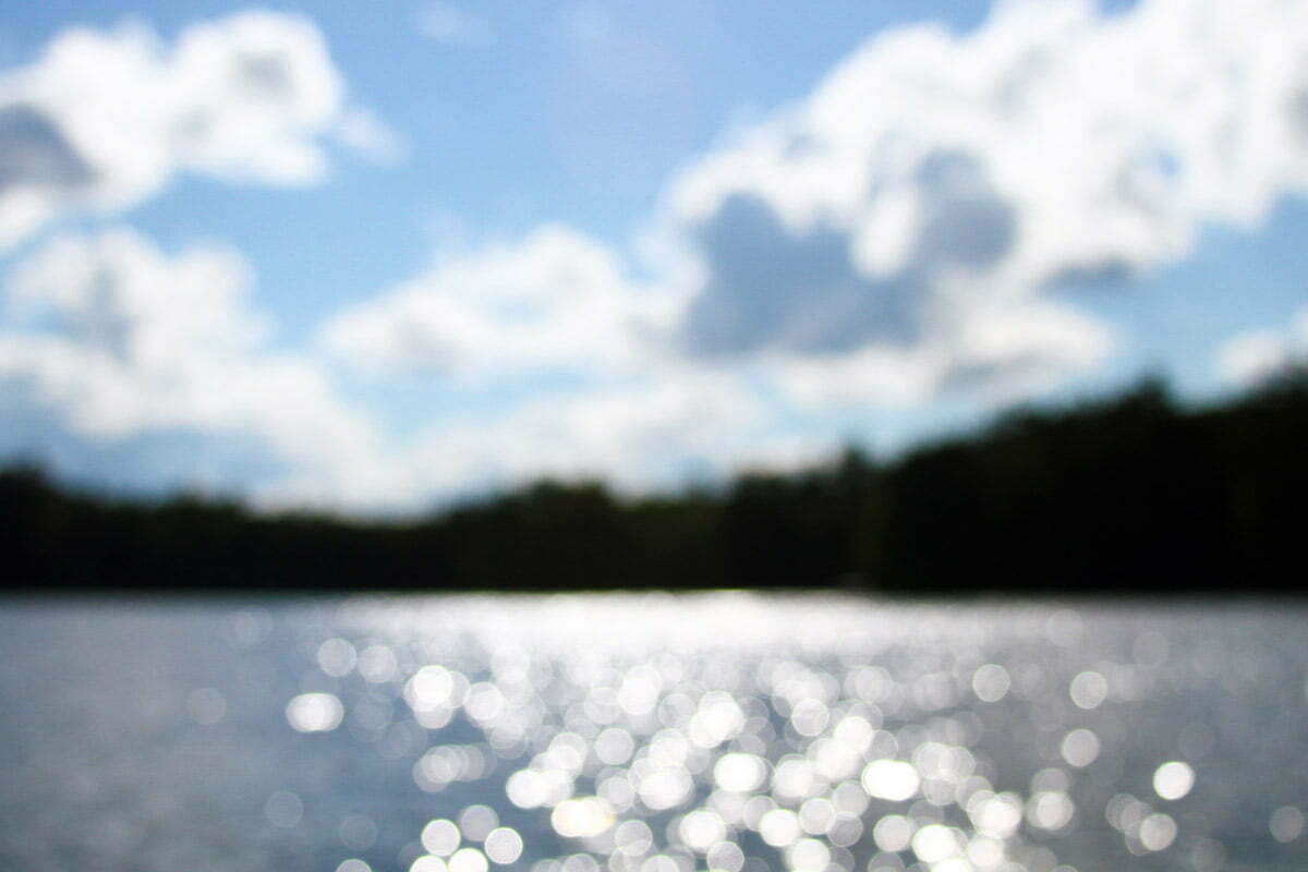 An abstract and out of focus shot of a cloudy sky, shimmering blue water and trees.
