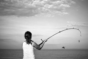 A woman casts the bait on her fishing pole into the water from the breakwater in Maine.