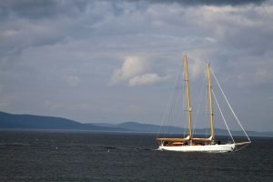 A two masted sailing ship off the coast of Maine with mountains and islands in the distance.