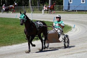 A grinning sulky driver in a green outfit drives his horse during a harness race in Maine.