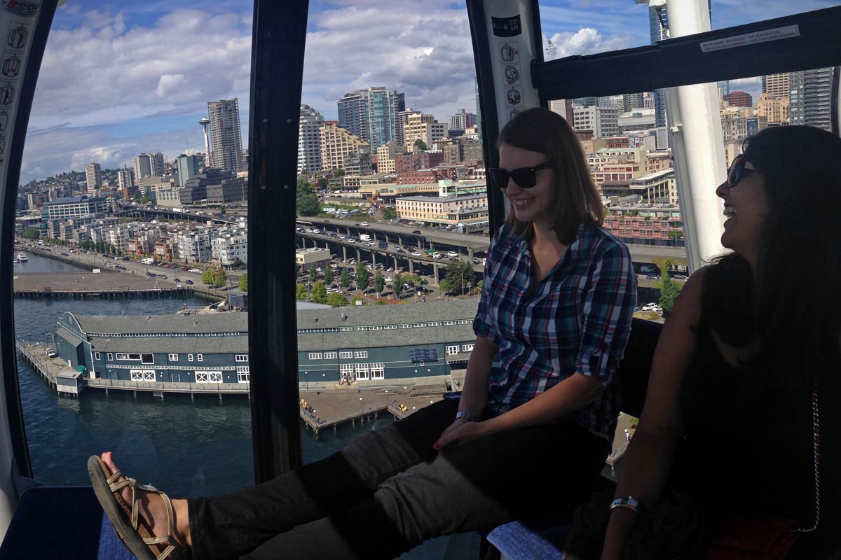 Two friends sit in the Seattle Great Wheel looking over the city from the ferris wheel compartment.