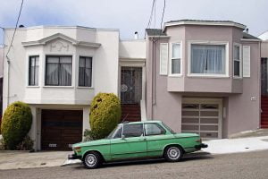 A slanted road in San Francisco with a parked green BMW 2002 sits outside two houses.
