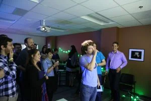 Eric smiles at looks at a projector screen while his coworkers look on.