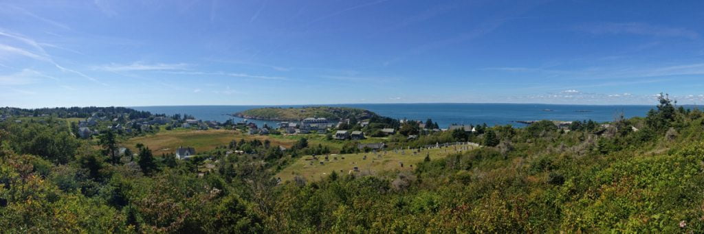 A panoramic photo of a blue sky and green landscape of the small rocky island of Monhegan off the coast of Maine.