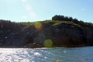 The rocky cliffs of Monhegan Island seen from the ocean on a sunny day in Maine.
