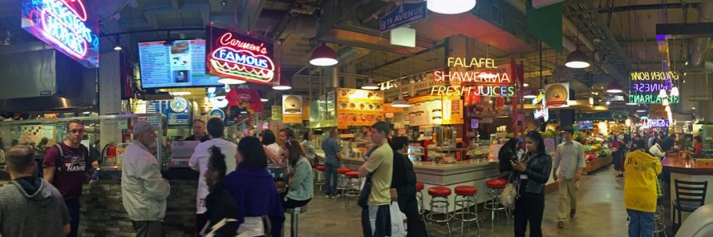 A panoramic photo of the Reading Terminal Market with a busy crowd and neon signs in Philadelphia, Pennsylvannia.
