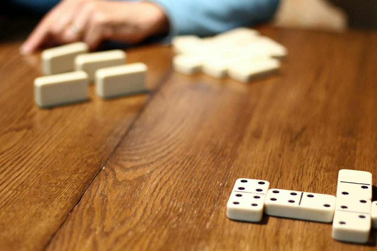 A game of dominoes takes place on a wood table.