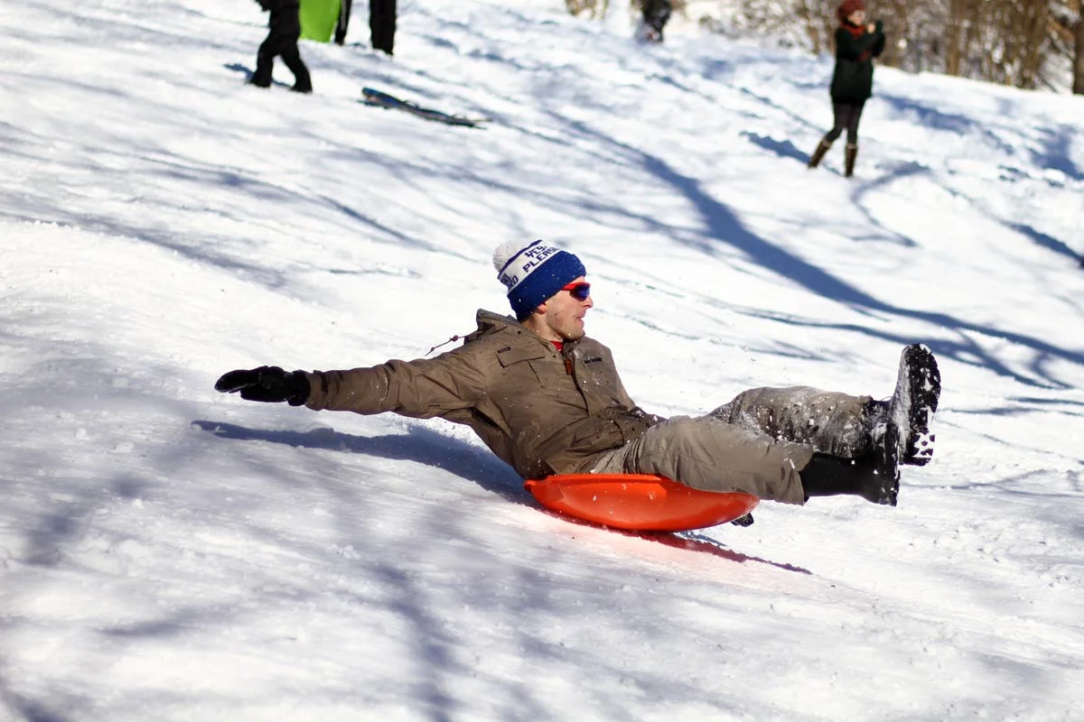 An adult on a plastic saucer sled reaches for balance going downhill in Washington DC during Winter Storm Jonas, also known as Snowzilla.