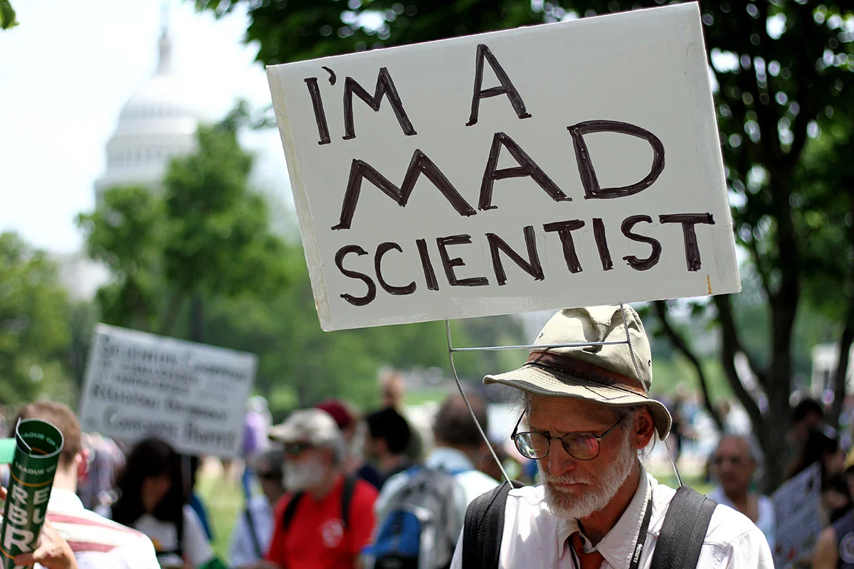 A man with a sign saying "I'm a mad scientist" at the People's Climate March in Washington DC with the US Capitol building in the background.
